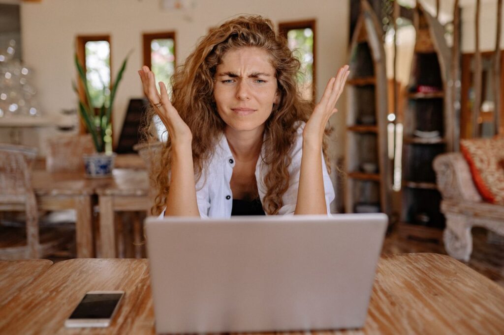A woman frustrated with her laptop while working remotely indoors, expressing stress.